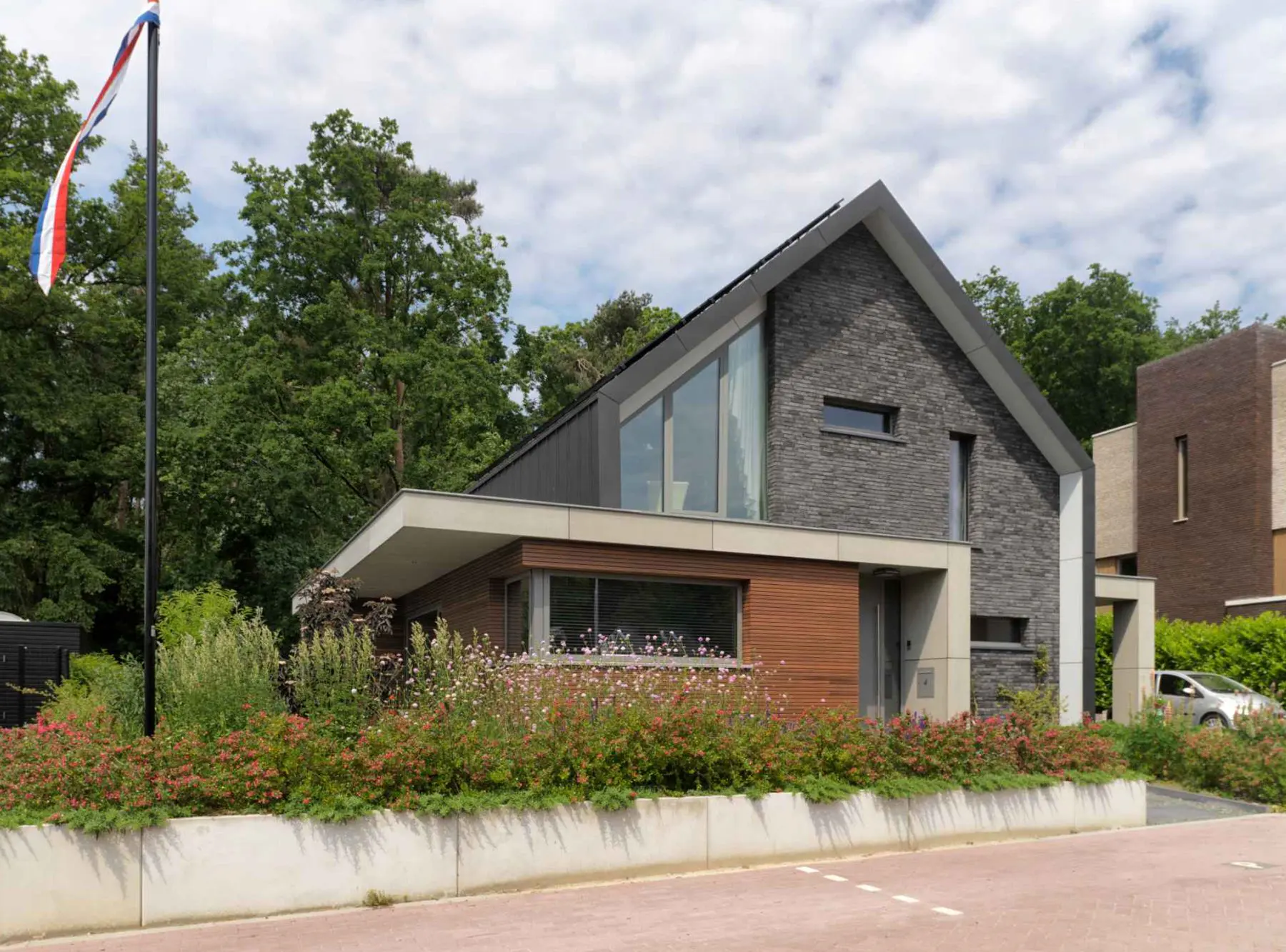 Vrijstaande woning met een hoge puntgevel van donkere steen en een strook glas tot in de nok